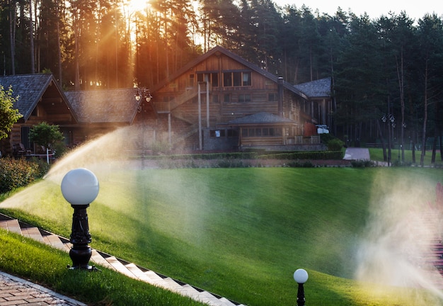 Molhando o gramado perto da casa de madeira em uma manhã de verão