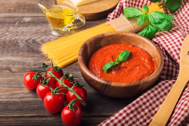 Molho caseiro marinara, macarrão espaguete, queijo parmesão, azeite, manjericão e tomate cereja em madeira rústica.