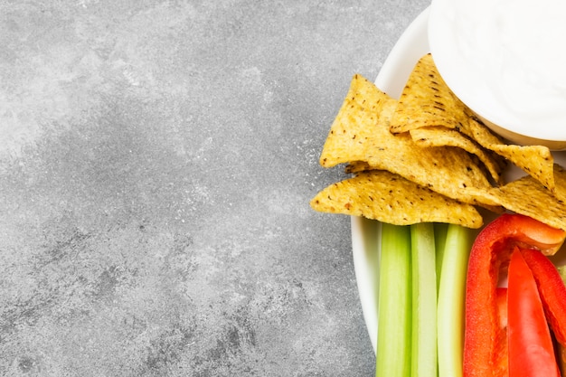 Molho cremoso em uma tigela branca, vários vegetais (aipo, pimenta) e nachos. Vista superior, copie o espaço. Fundo de alimentos