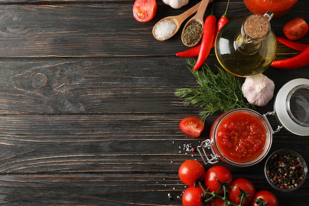 Molho de pimenta, alho, tomate cereja, azeite, especiarias sobre fundo de madeira, espaço para texto. Vista do topo