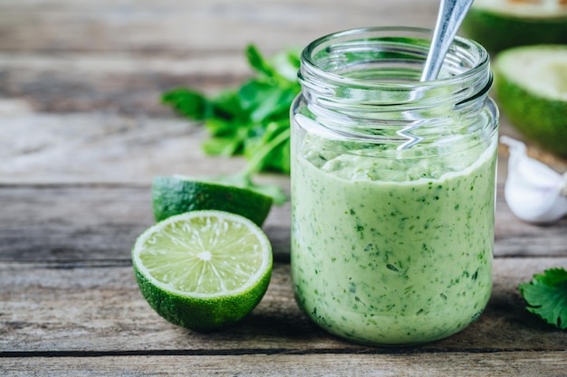 Molho de salada verde com limão de abacate e coentro em uma jarra de vidro em um fundo rústico