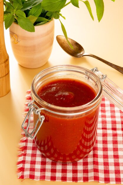 Molho de tomate fresco em uma jarra de vidro com folhas de manjericão tomate fatiado em um fundo bege na vista frontal