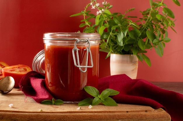 Molho de tomate fresco em uma jarra de vidro em uma mesa de madeira e um fundo vermelho na vista frontal