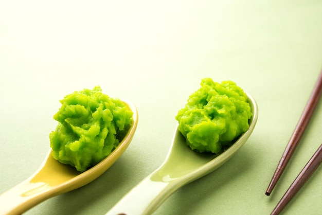 Molho de wasabi verde ou pasta em uma tigela, com pauzinhos ou colher sobre um fundo colorido simples. foco seletivo