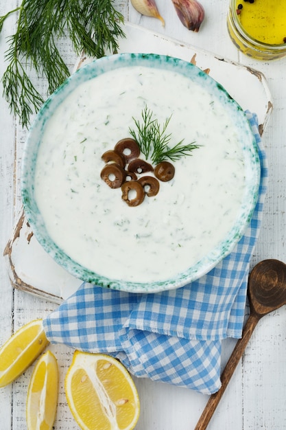 Molho grego tradicional Tzatziki. Iogurte, pepino, endro, alho e óleo de sal em uma tigela de cerâmica sobre uma superfície de madeira clara