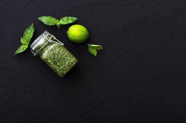 Molho pesto caseiro, manjericão verde, limão em fundo escuro de cimento. molho pesto verde italiano em frasco de vidro para macarrão, espaguete. alimentação vegetariana saudável. vista superior, plana leiga com espaço de cópia para o texto.