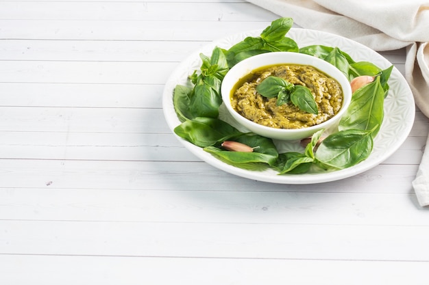 Foto molho pesto em um prato e folhas frescas de manjericão com alho. copie o espaço