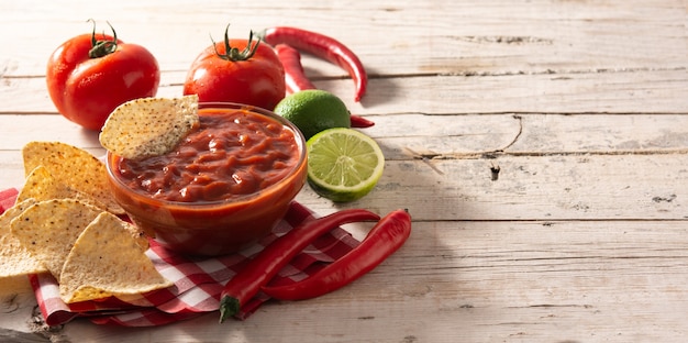 Foto molho picante de pimenta em uma tigela com chips de nacho na mesa de madeira