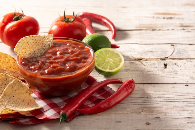 Foto molho picante de pimenta em uma tigela com chips de nacho na mesa de madeira