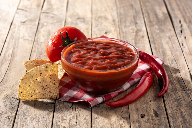 Molho picante de pimenta em uma tigela com nacho chips na mesa de madeira