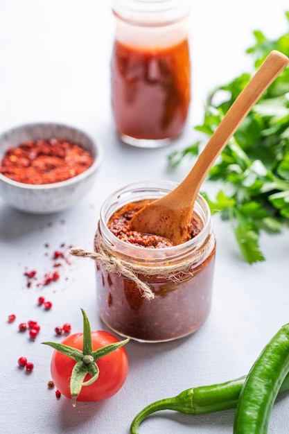 Molho quente adjika Aperitivo caseiro com pimenta e tomate em uma jarra sobre fundo claro com ervas frescas e legumes fechados