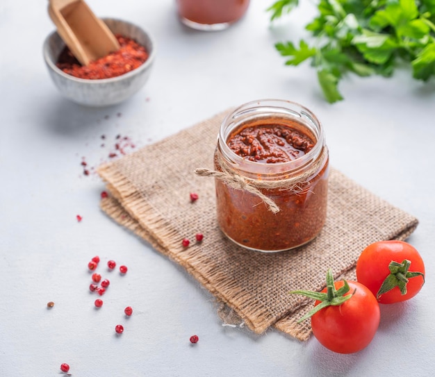 Molho quente adjika Aperitivo caseiro com pimenta e tomate em uma jarra sobre fundo claro com ervas frescas e legumes