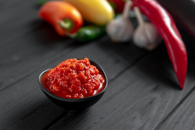 Molho vermelho de pasta de pimenta quente sobre fundo de madeira ajika ou ajika na cozinha georgiana ou hariss