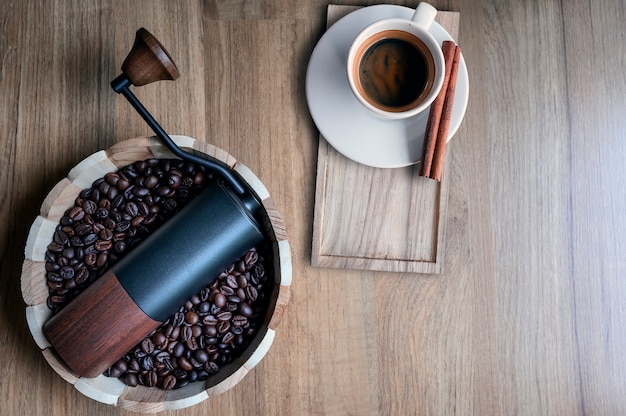 Molinillo de café en un cubo de madera con granos de café y una taza de café en la mesa de madera