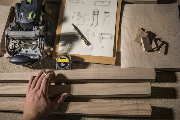 Molino de ranura, lápiz y cinta métrica, espacios en blanco de madera y mano de carpintero con un cigarrillo