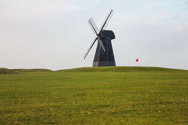 Molino de viento y bandera roja con césped verde y cielo nublado en el campo de golf Rottingdean Windmill. Sussex del Este, Inglaterra.