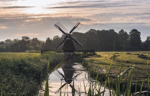molino de viento de madera junto al agua en un campo en los Países Bajos