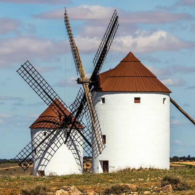 Molinos de viento blancos viejos, hechos de piedra, en el campo con cielo azul y nubes blancas. La Mancha, Castilla, España. Europa.