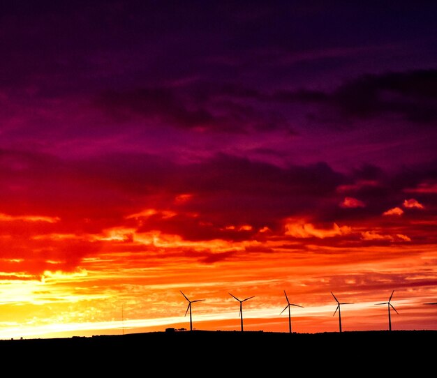 Molinos de viento de fondo con un atardecer de varios colores (naranja, rojo y violeta)