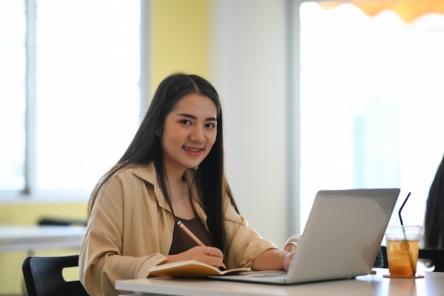 Mollige Studentin lernt online und macht sich Notizen, während sie Online-Fernbildung erhält.