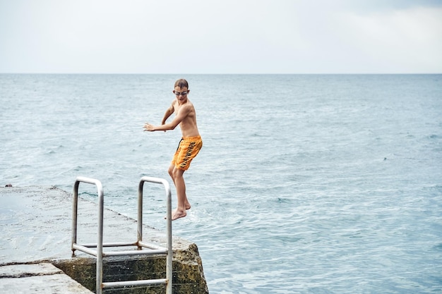 Momente eines Jungen, der von einem Steinpier mit einer Leiter ins Meer springt und Tricks in einer kombinierten Bildsequenz macht