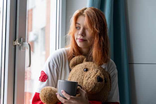 Momento acogedor de la Generación Z Adolescente pelirroja con bebida caliente y oso de peluche