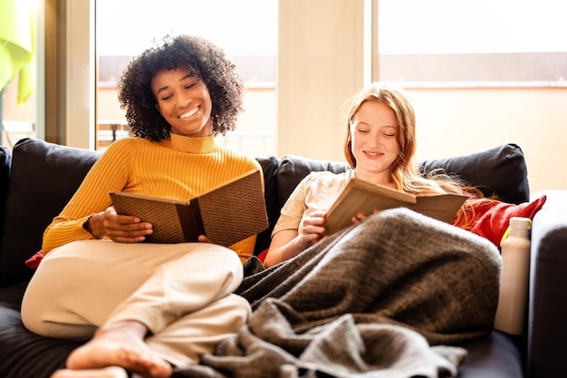 Momento de felicidade da vida doméstica do casal lgbt, duas jovens felizes sentadas no sofá lendo livros, estilo de vida do casal lésbica geração z