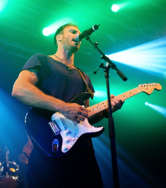 En el momento glorioso Músico atractivo tocando su guitarra en un concierto