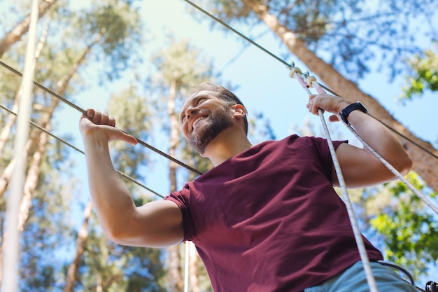 Momento de su vida. Joven emocionado divirtiéndose en un parque de cuerdas y sonriendo alegremente mientras camina por el sendero