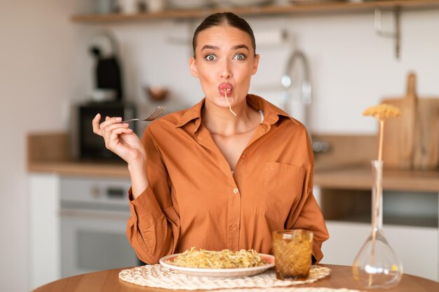 Momentos culinários alegres senhora emocional engraçada provando delicioso espaguete caseiro sentado à mesa