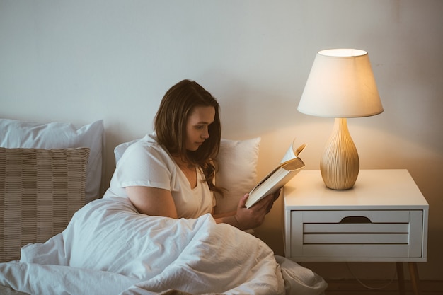 Momentos do estilo de vida de uma jovem em casa. Mulher lendo antes de dormir