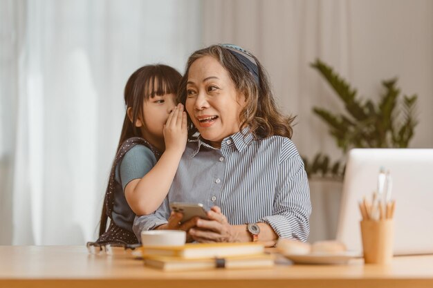 Momentos felizes da neta dão abraço enquanto mulher de negócios sênior asiática trabalhando em casa Conceito de família