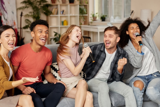 Momentos llenos de música emocionados jóvenes amigos multiculturales jugando karaoke en casa cantando con