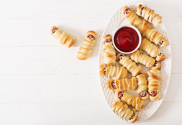 Momias de salchicha de miedo en la masa con ojos divertidos en la tabla. Comida de Halloween