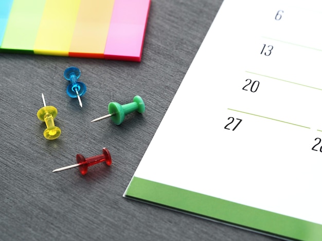Foto monatlicher kalender, freigesetzte push-pins und farbige seitenmarkierungen auf einem tisch, zeitmanagementkonzept