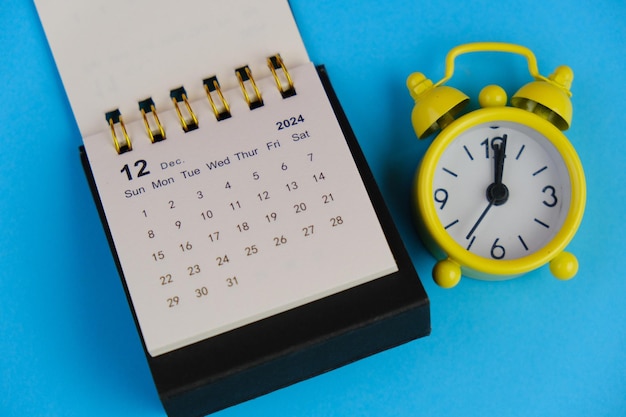 Monatlicher Schreibtischkalender für Dezember 2024 auf einem Holztisch mit Wecker