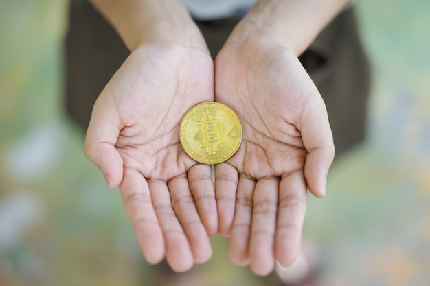 Moneda de bitcoin dorada en manos de mujeres.