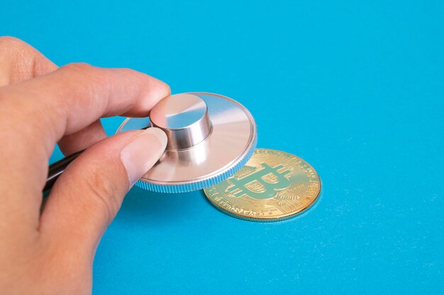 Moneda Bitcoin y estetoscopio sobre fondo azul.