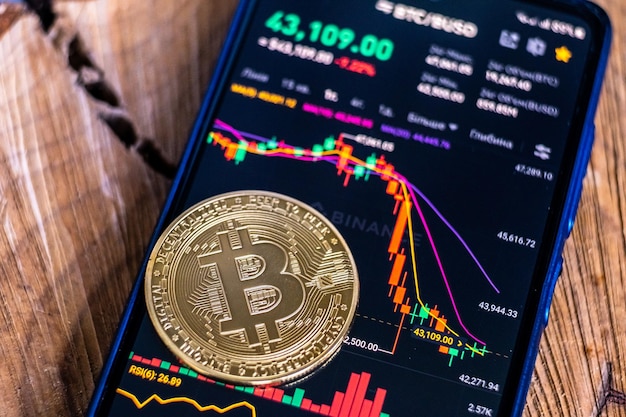 Moneda de Bitcoin en el fondo de la pantalla de un teléfono inteligente con un gráfico de caída del mercado de criptomonedas en el intercambio de Binance
