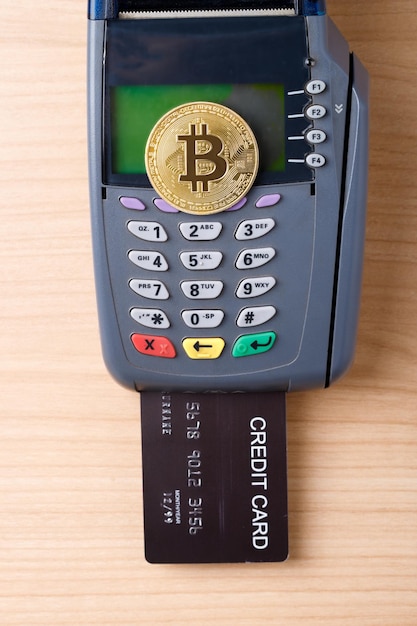 Moneda criptográfica BTC estándar de Bitcoin en dispositivo de máquina de tarjeta de crédito Maqueta de vista superior en mesa de madera
