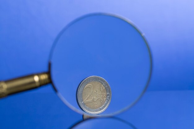 Moneda de dos euros sobre fondo azul a través de la lupa con bonito reflejo