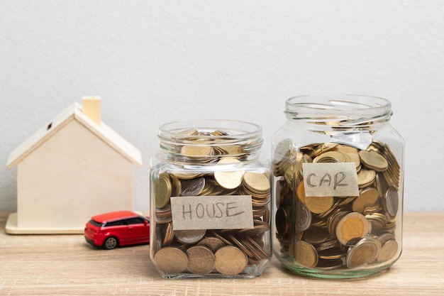 Moneda en un frasco de vidrio para ahorrar dinero y casa de madera y coche rojo sobre la mesa, concepto financiero