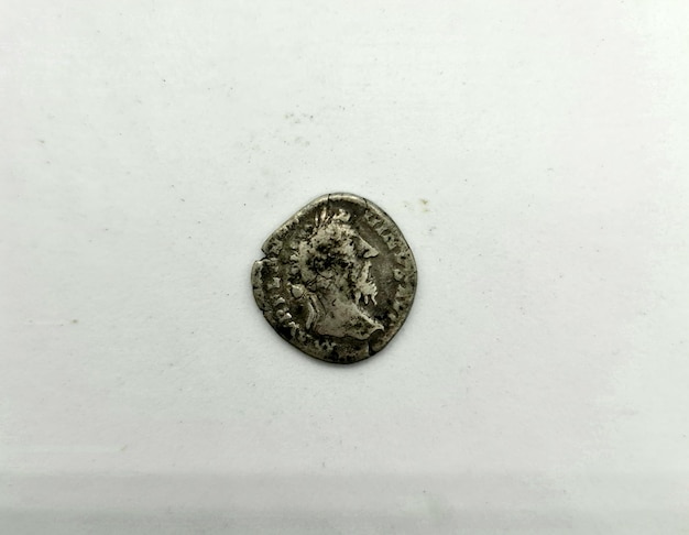 Una moneda del imperio romano está sobre una superficie blanca.