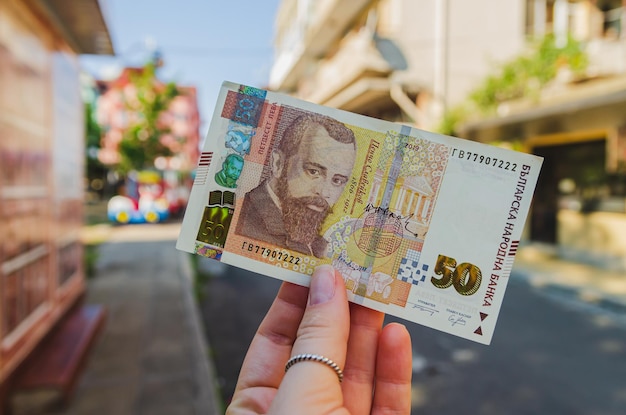 Foto moneda lev búlgaro la mano de una mujer sostiene un billete de 50 denominaciones en la calle pago de bienes y servicios