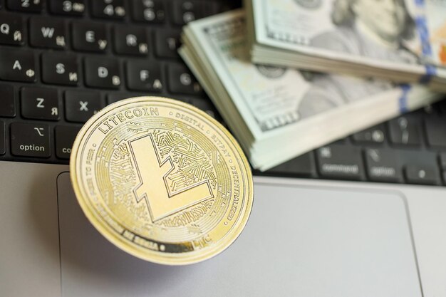 Moneda Litecoin LTC con una gran cantidad de billetes de cien dólares estadounidenses en la superficie de la computadora portátil