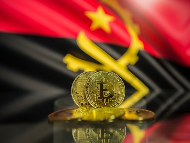 Moneda de oro Bitcoin y bandera desenfocada de fondo de Angola. Concepto de criptomoneda virtual.