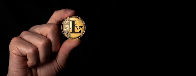 Moneda de oro Litecoin en mano masculina sobre fondo negro. Banner con espacio para texto.