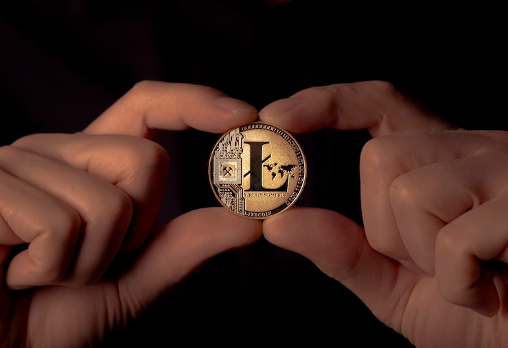 Foto moneda de oro litecoin en mano masculina sobre fondo negro.