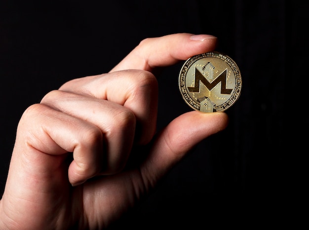 Moneda de oro Monero en mano masculina sobre fondo negro.