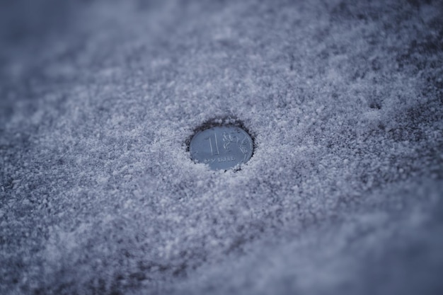 Moneda de rublo entre nieve sucia y cenizas